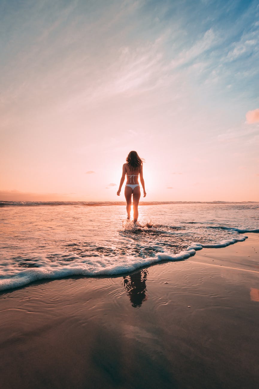 back view of a woman in white bikini standing on the beach during golden hour