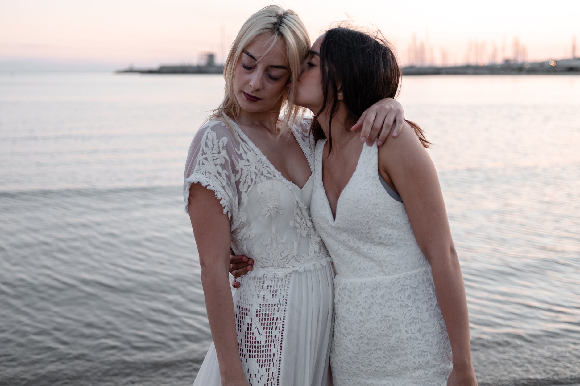 woman kissing woman while standing near body of water