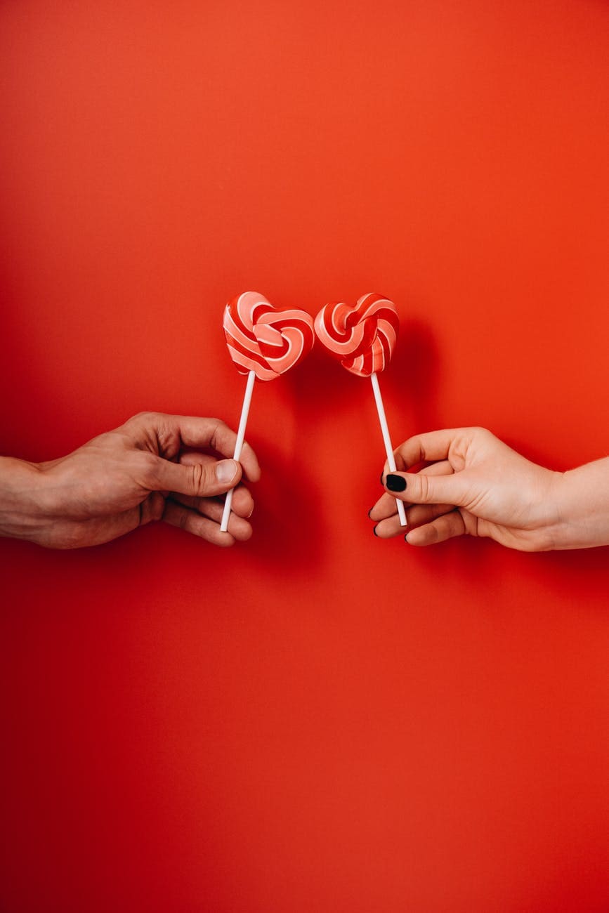 two hands holding heart shaped lollipops