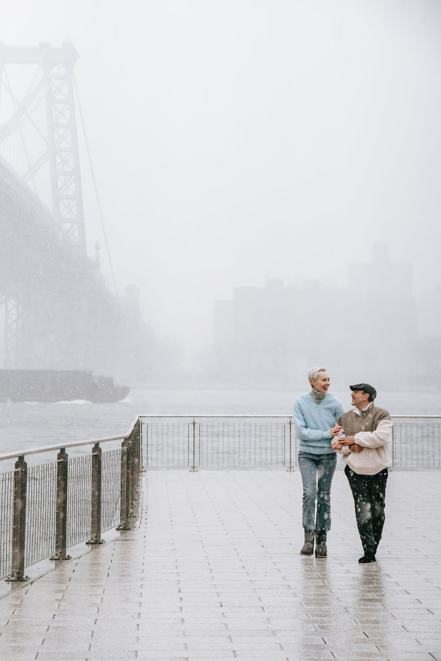 couple walking on embankment near river and bridge in winter