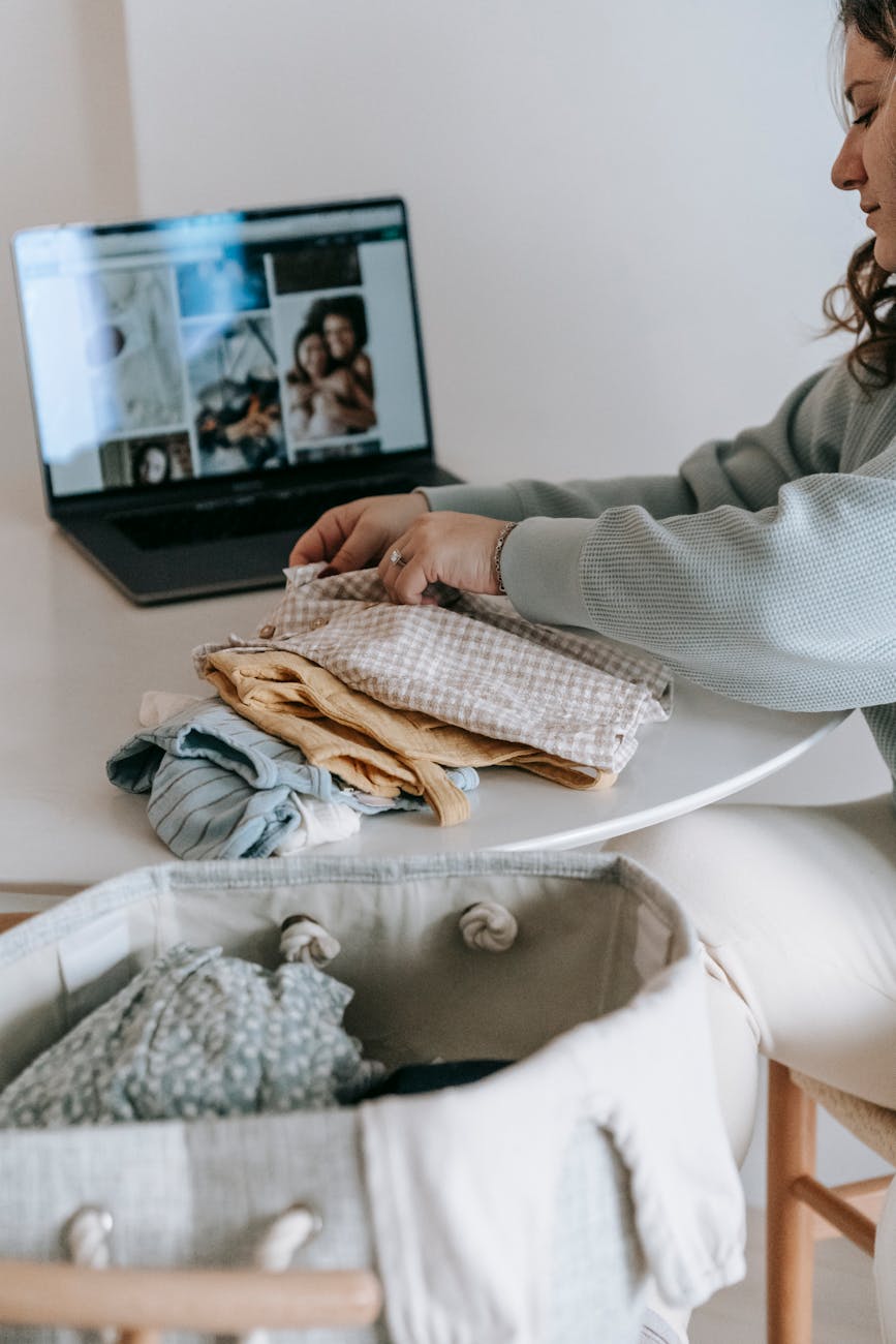 woman folding baby clothes near laptop